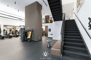 Ein Fitnessraum mit Trainingsgeräten, einer Treppe und einem Schild mit Raumangaben.