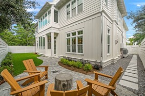 A two-story house with a covered patio area featuring wooden chairs and a central wooden stump. - Grace By The Sea|Easy Beach Access|Private Pool|Golf Cart (Seacrest Beach)