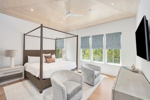 Een moderne slaapkamer met een hemelbed, twee fauteuils, een nachtkastje met lamp en een groot raam met gordijnen.