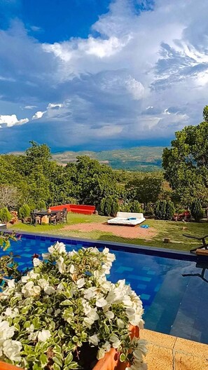 Une piscine offrant une vue sur un bâtiment aux toits rouges et sur une végétation luxuriante en arrière-plan.