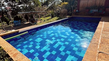 Una piscina con diseño de cuadros, rodeada por una terraza de madera y un jardín.