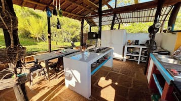 Un área de cocina al aire libre con estufa a gas, refrigerador y mesa con sillas.