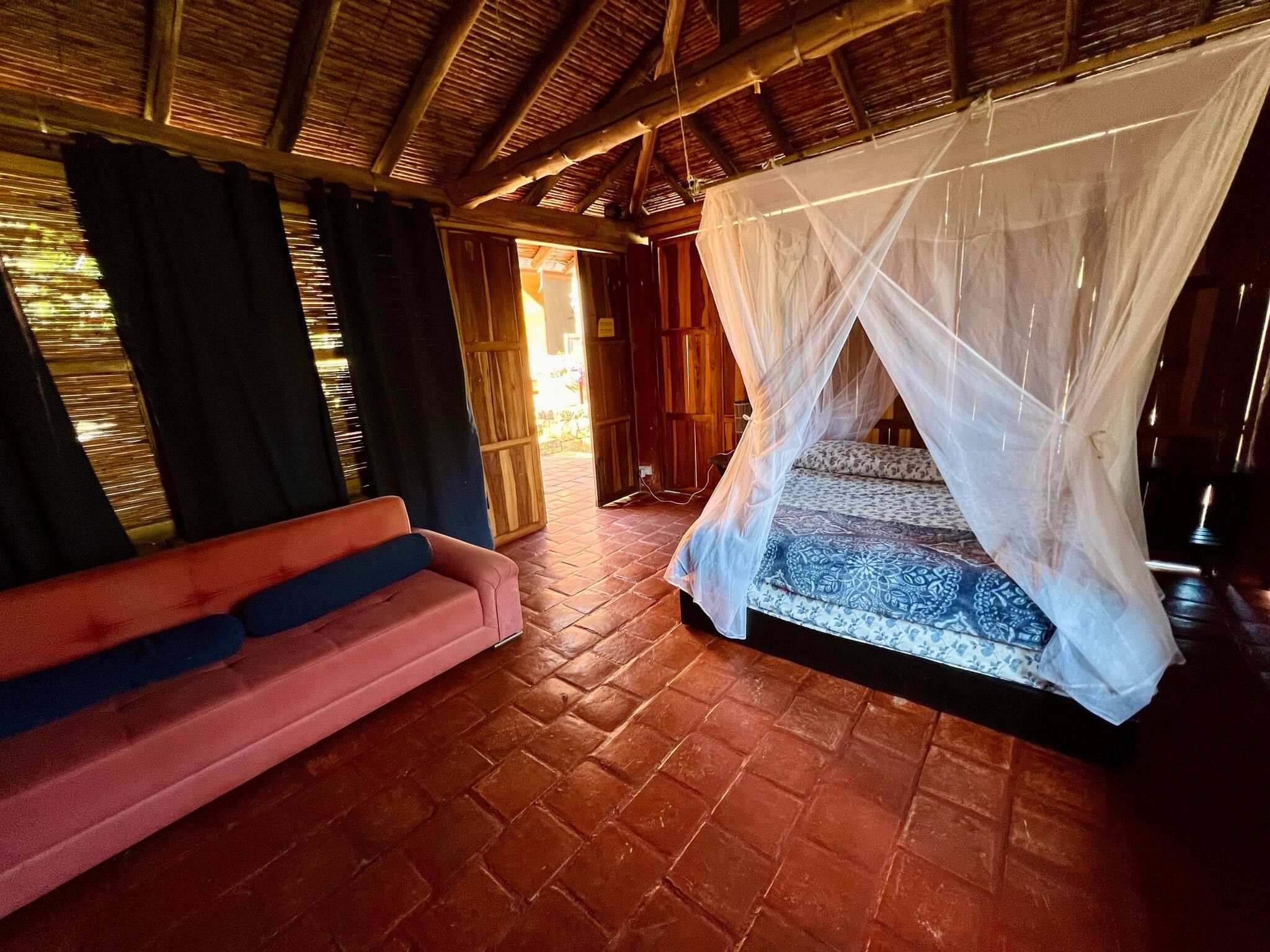 A room with a bed under a canopy, a sofa, and a wooden ceiling.