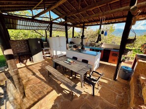 An outdoor kitchen area with a dining table and chairs, surrounded by stone flooring and a wooden pergola. - Casa upa con Piscina Climatizada (Barichara)