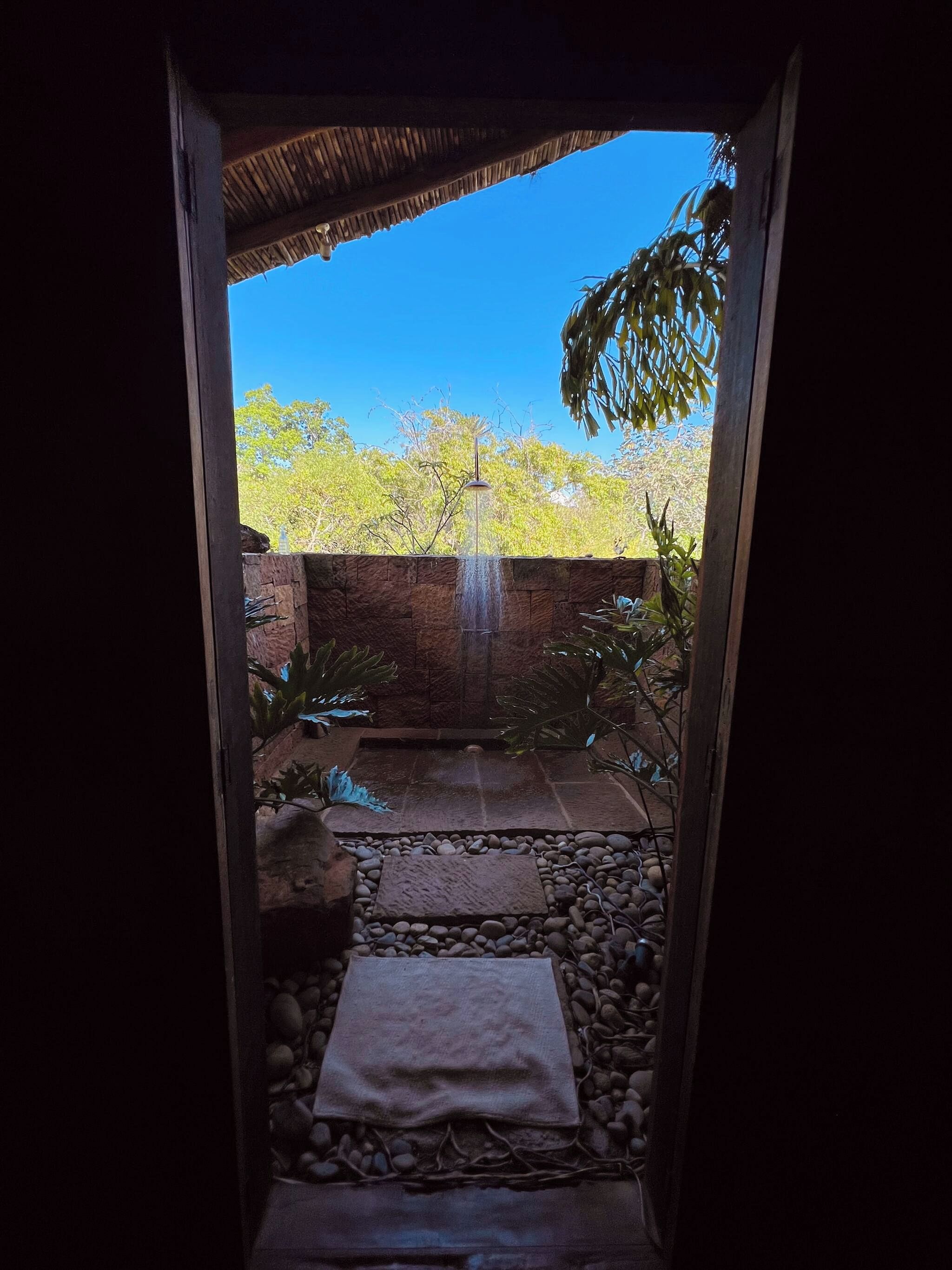 A stone pathway leading to a water feature with a thatched roof overhead.