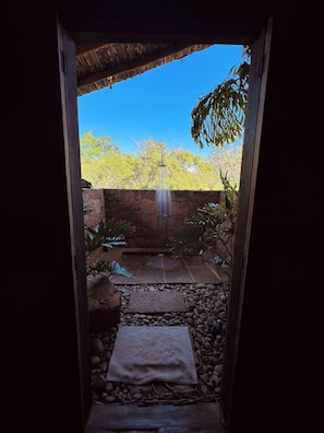 A stone pathway leading to a water feature with a thatched roof overhead.