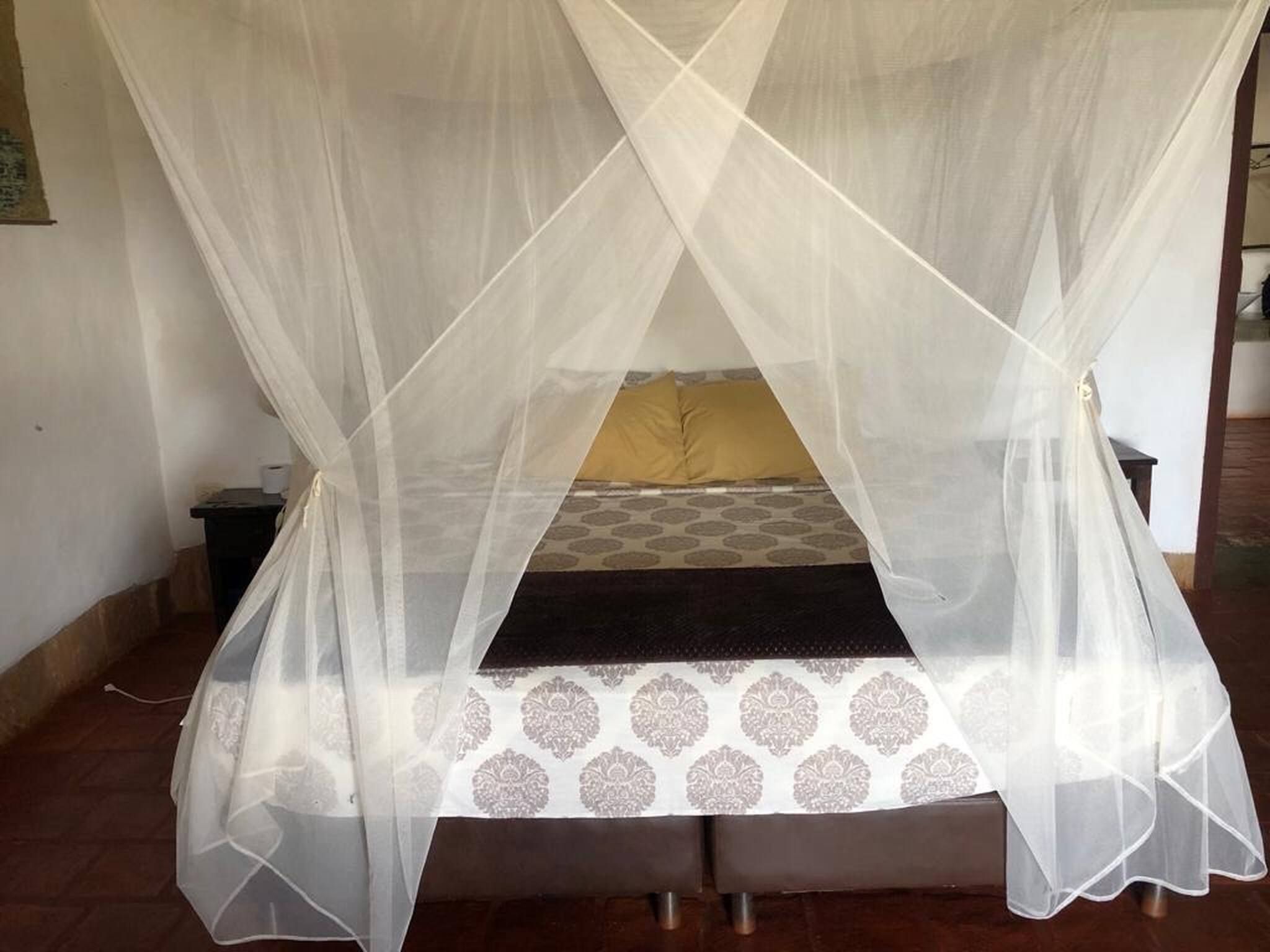 Uma cama com dossel, colcha estampada e um único travesseiro amarelo.