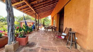 Uma área externa coberta com teto de madeira, piso de pedra e plantas em vasos.