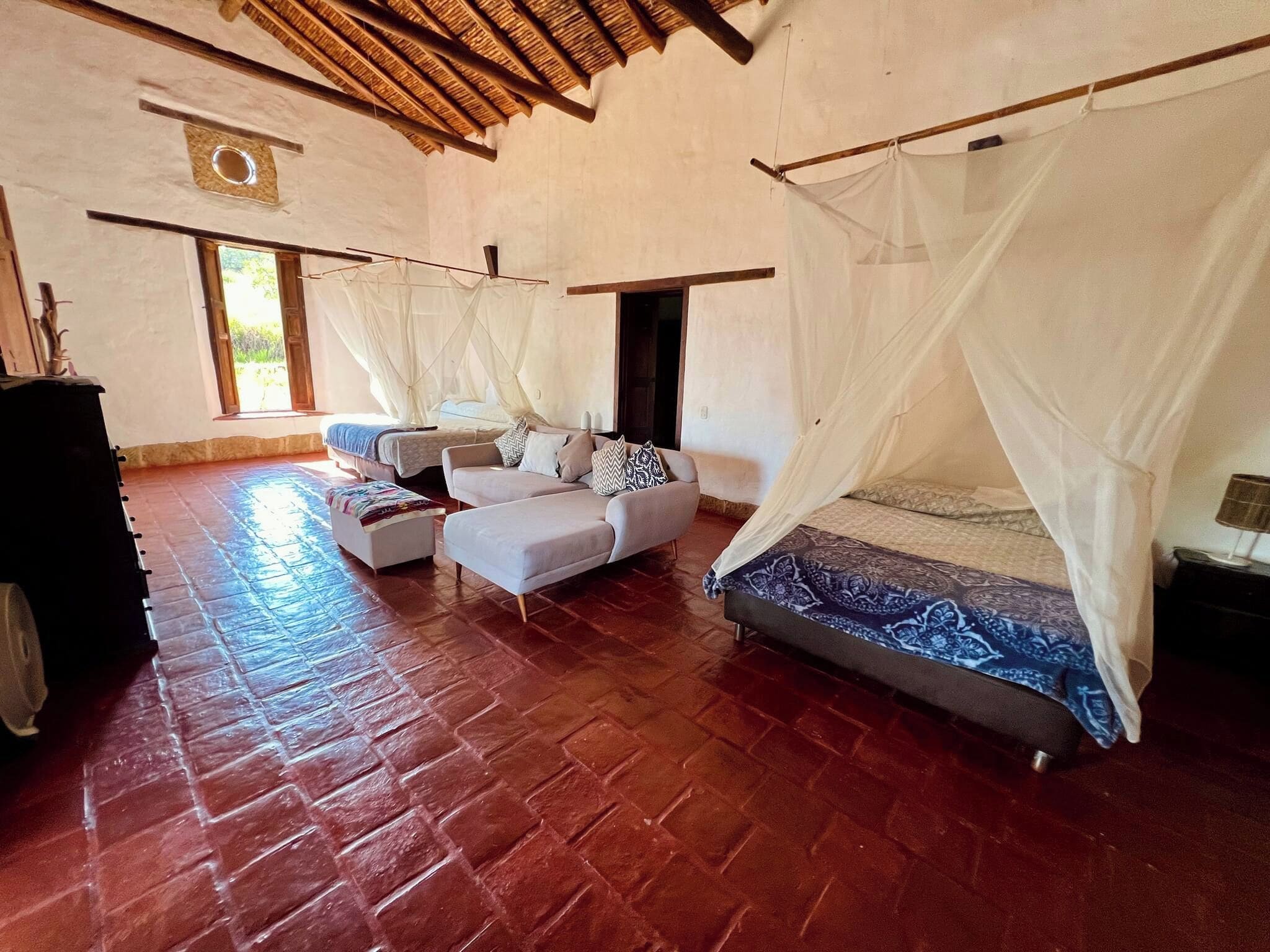 Un'ampia stanza con un letto grande, una poltrona e un tavolino. Una finestra offre luce naturale e vista sull'esterno.