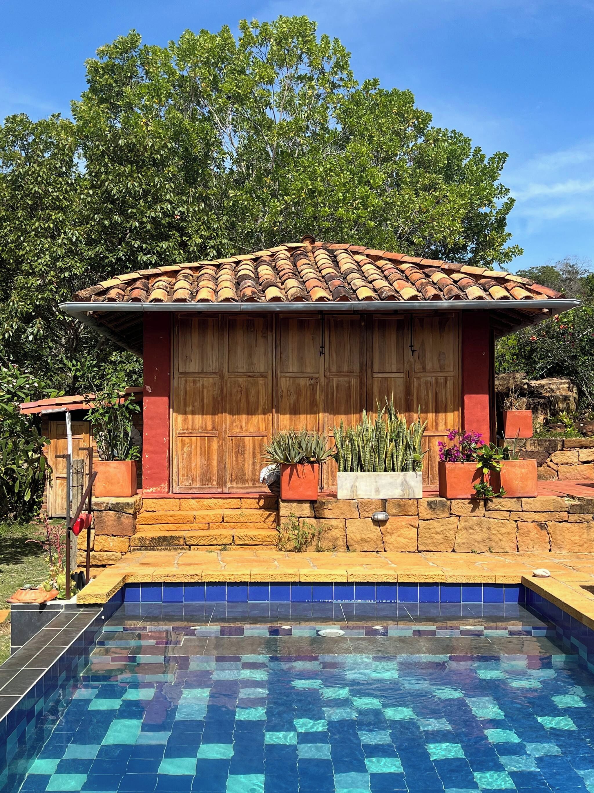 A pool with blue tiles, a wooden building with a tiled roof, and potted plants.