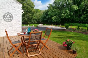 An outdoor patio with a table and chairs, a decorative wall, and a garden with a stone fountain.