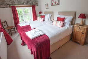 Een tweepersoonsbed met rode en witte beddengoed, een houten nachtkastje en een stoel.