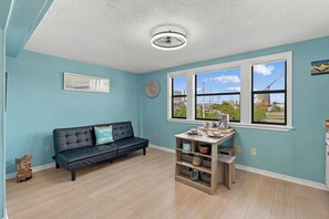 A room with a blue wall, a black leather sofa, a wooden table, and a ceiling fan. - 1209C - Large Studio Walking Distance to Beach (Panama City)