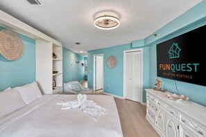 Une chambre d’hôtel équipée d’un lit, d’une coiffeuse avec un miroir, d’un ventilateur de plafond et d’un téléviseur fixé au mur qui diffuse des publicités pour « FUNQUEST Vacation Rentals ».