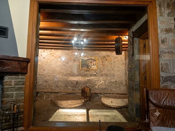 A stone-walled room with a wooden ceiling, a framed picture on the wall, and a bench.