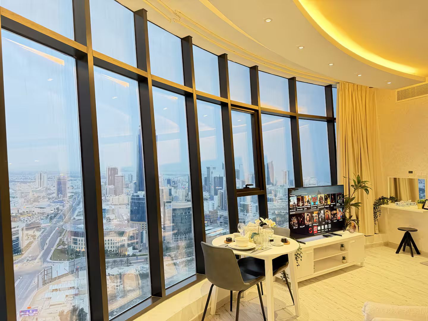 A modern room with large windows, a dining area, and a television.