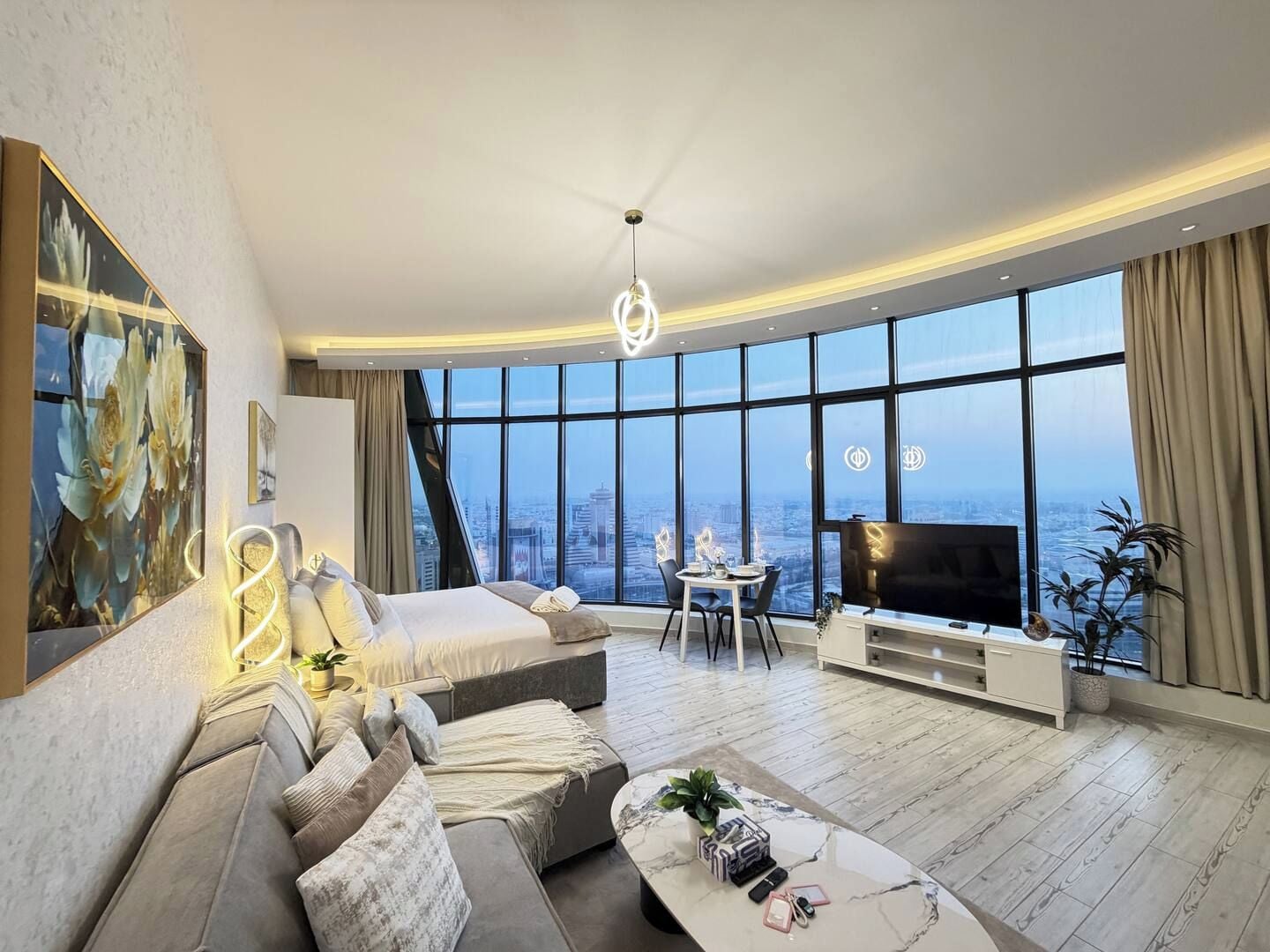 A modern living room with a large bed, a sofa, a dining area, and a TV.