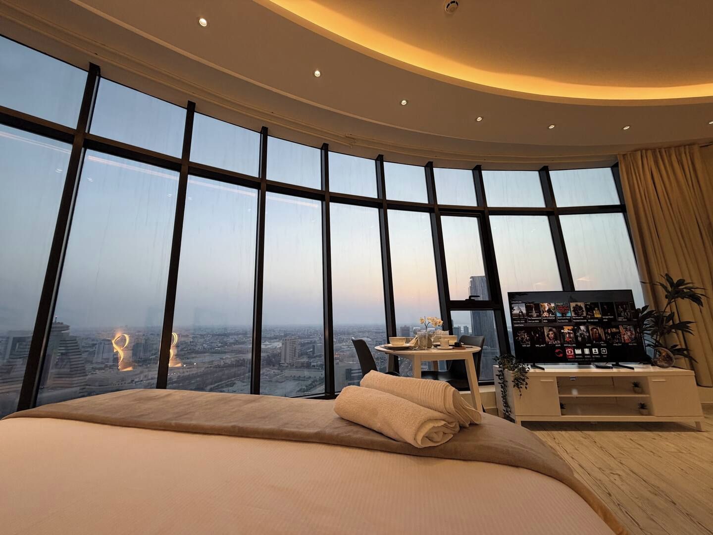 A high-rise hotel room with a large bed, a small table, and a TV.