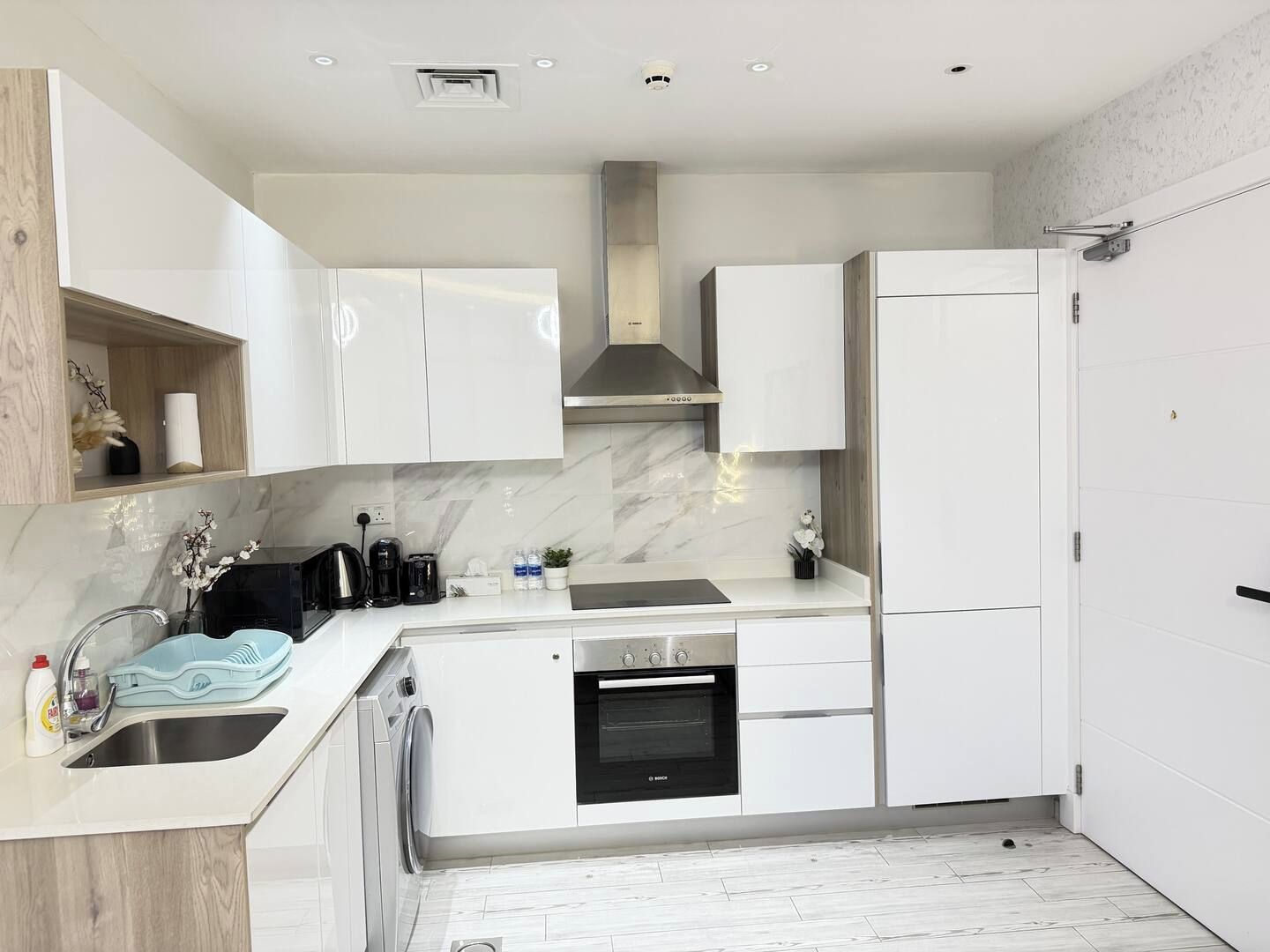 A modern kitchen with white cabinetry, a built-in oven, and a stainless steel range hood.