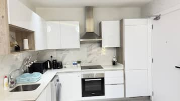 A modern kitchen with white cabinetry, a built-in oven, and a stainless steel range hood.