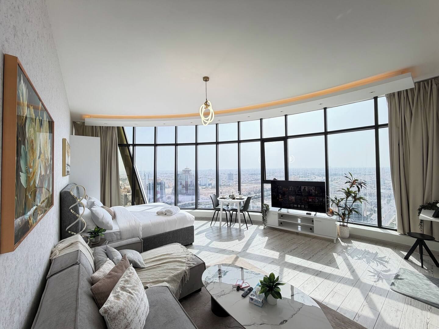 A modern hotel room with a large bed, a sofa, a TV, and a city view.