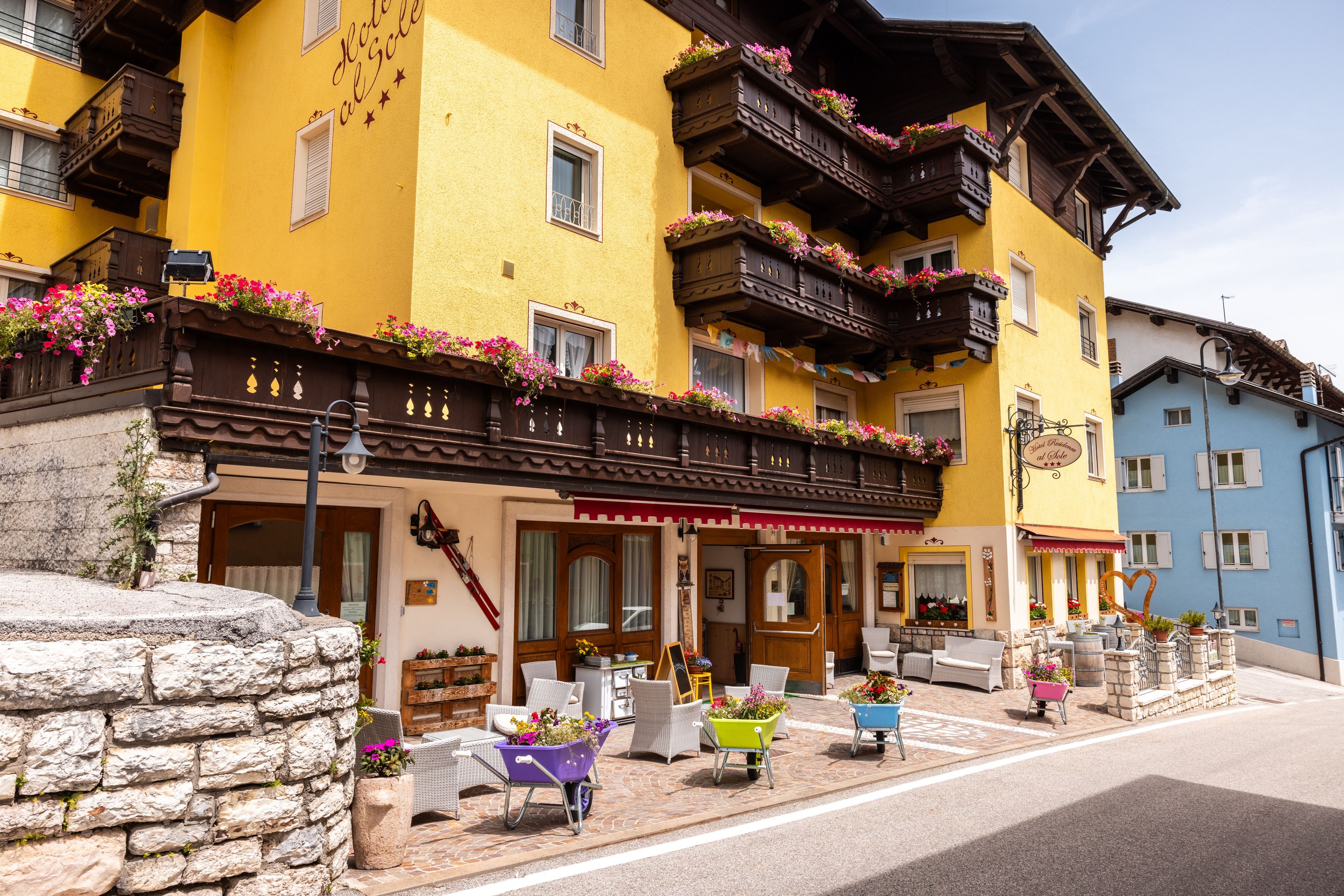 Un hôtel à la façade jaune, doté de balcons en bois ornés de jardinières, de places assises en plein air et de murs en pierre.