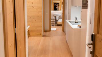Un pasillo con piso de madera que conduce a una cocina con armarios blancos y un microondas empotrado.