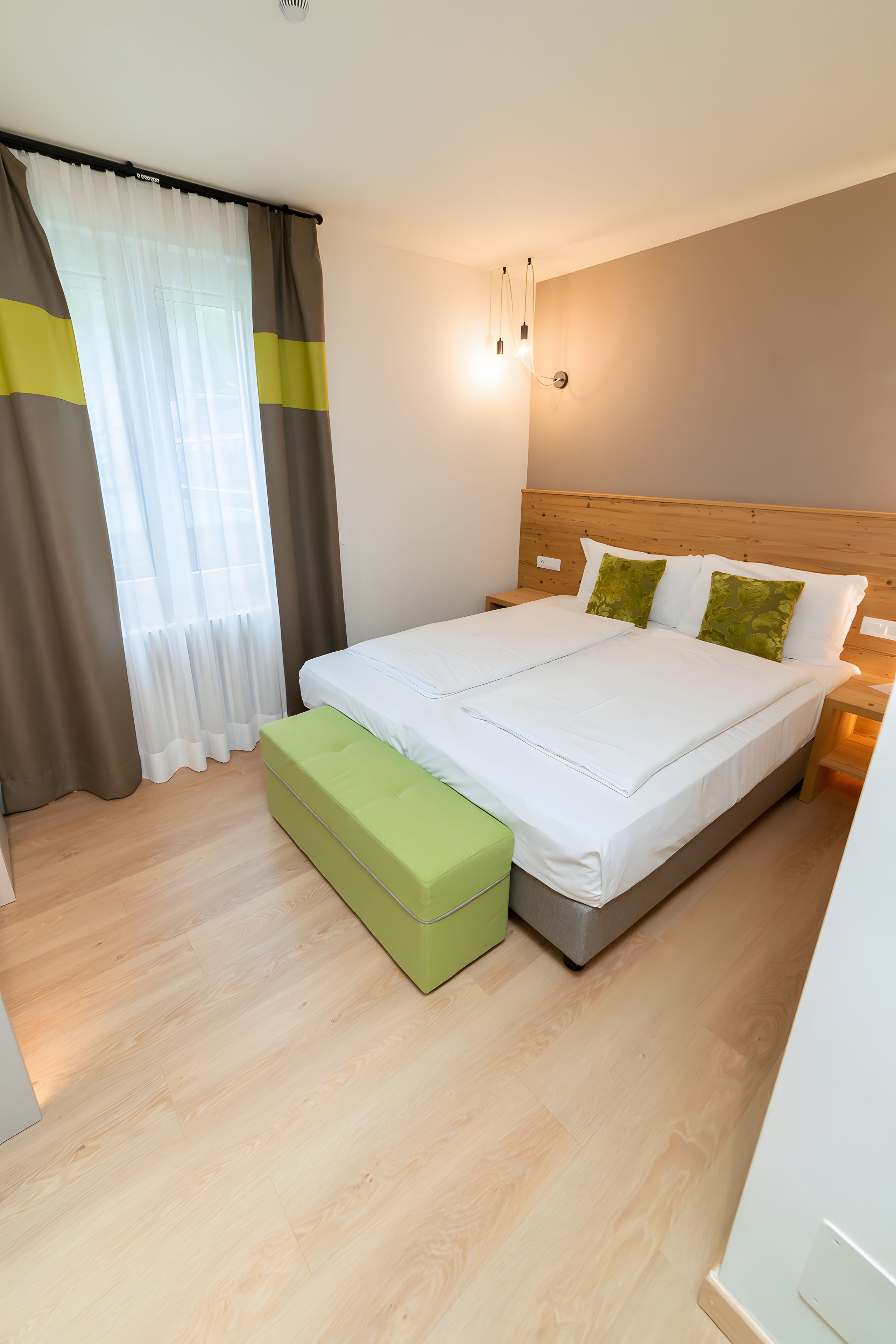Habitación de hotel con cama, una banca, una mesita de noche y una lámpara de pared.