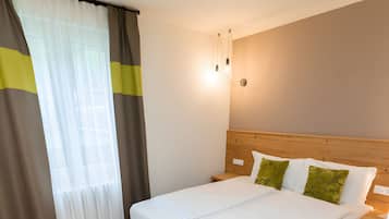 Habitación de hotel con cama, una banca, una mesita de noche y una lámpara de pared.