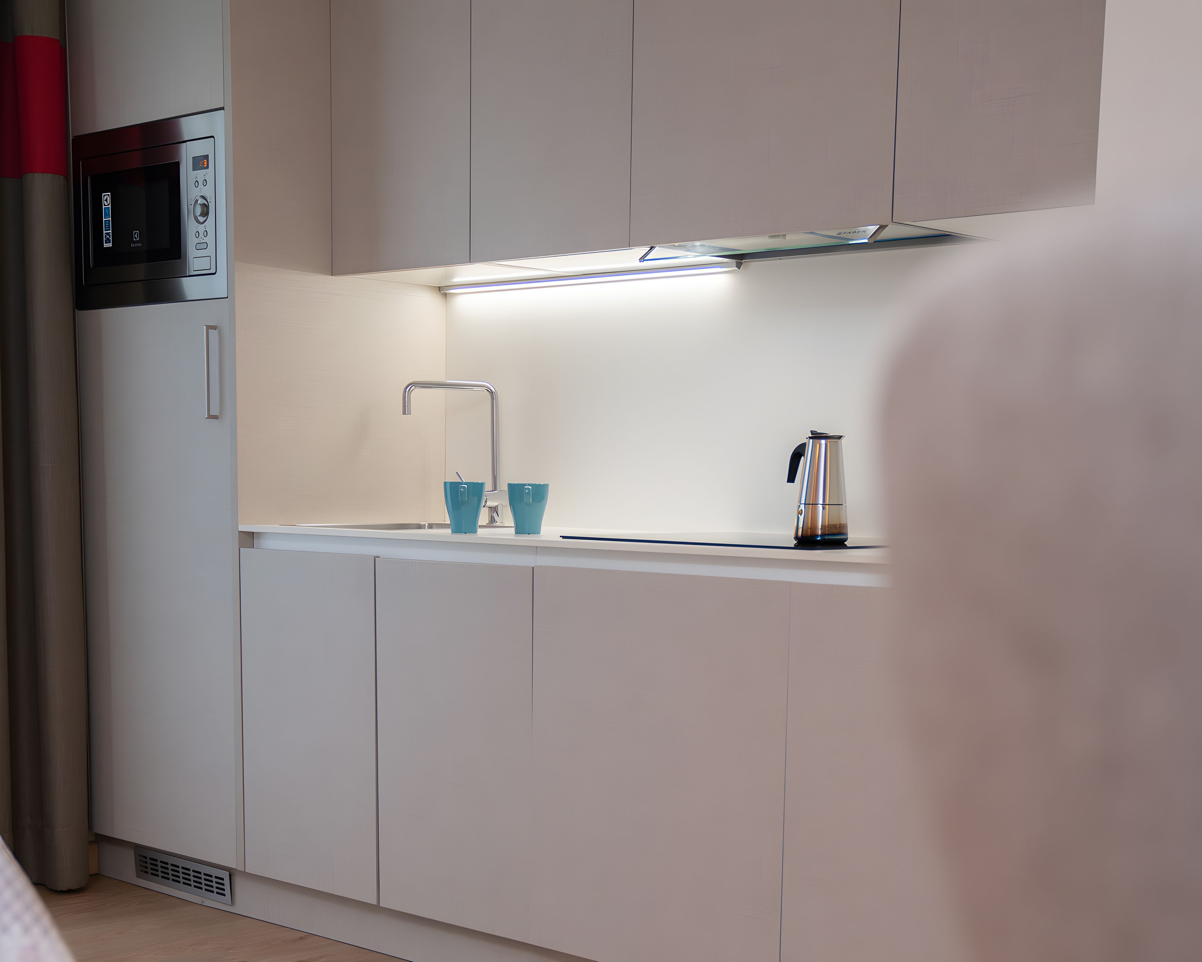 Una cocina moderna con microondas, un lavamanos y una tetera.