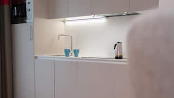 Una cocina moderna con microondas, un lavamanos y una tetera.