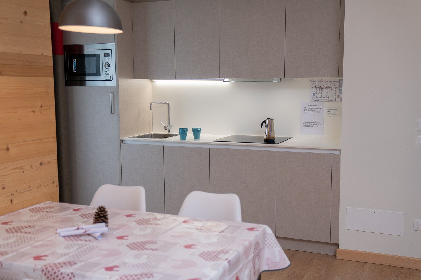 Une cuisine moderne équipée d’un four à micro-ondes encastré, d’une bouilloire et d’un évier. On y trouve une table à manger avec des chaises et un cône de pin décoratif.