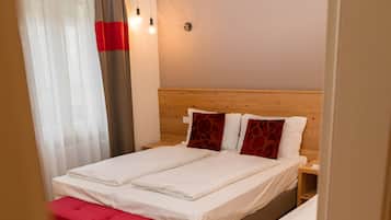 Un dormitorio con una cama doble, un reposapiés rojo, una mesita de noche de madera y una lámpara de pared.