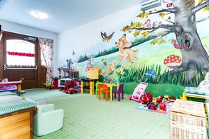 Un cuarto de juegos infantil con un mural, juguetes y una alfombra verde.