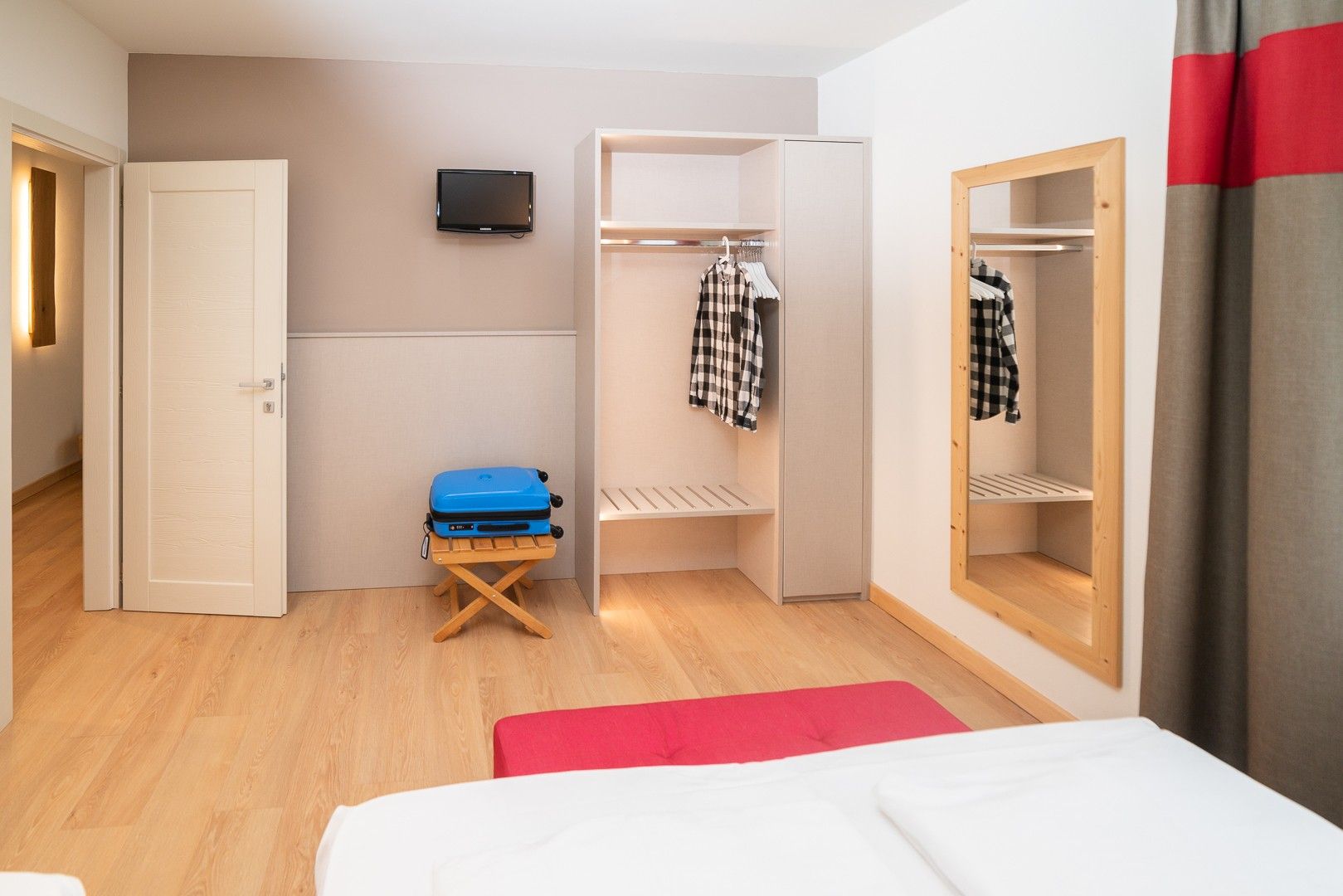 Una habitación de hotel compacta con cama, un pequeño espacio de descanso, un armario, televisor y espejo.