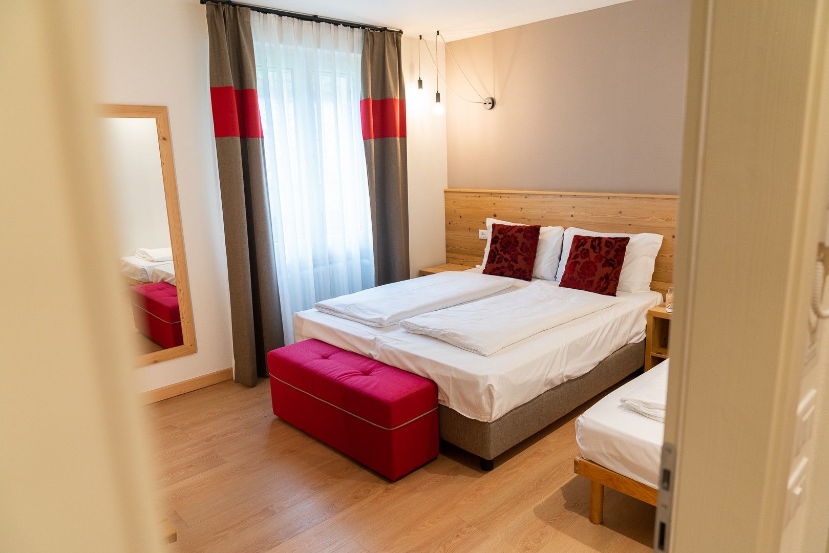 Une chambre d’hôtel avec un lit double, un banc rouge, une tête de lit en bois et un miroir au mur.
