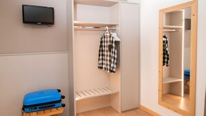 Hotellihuone, jossa on sänky, punainen matto, sininen matkalaukku, televisio, vaatekaappi ja peili.