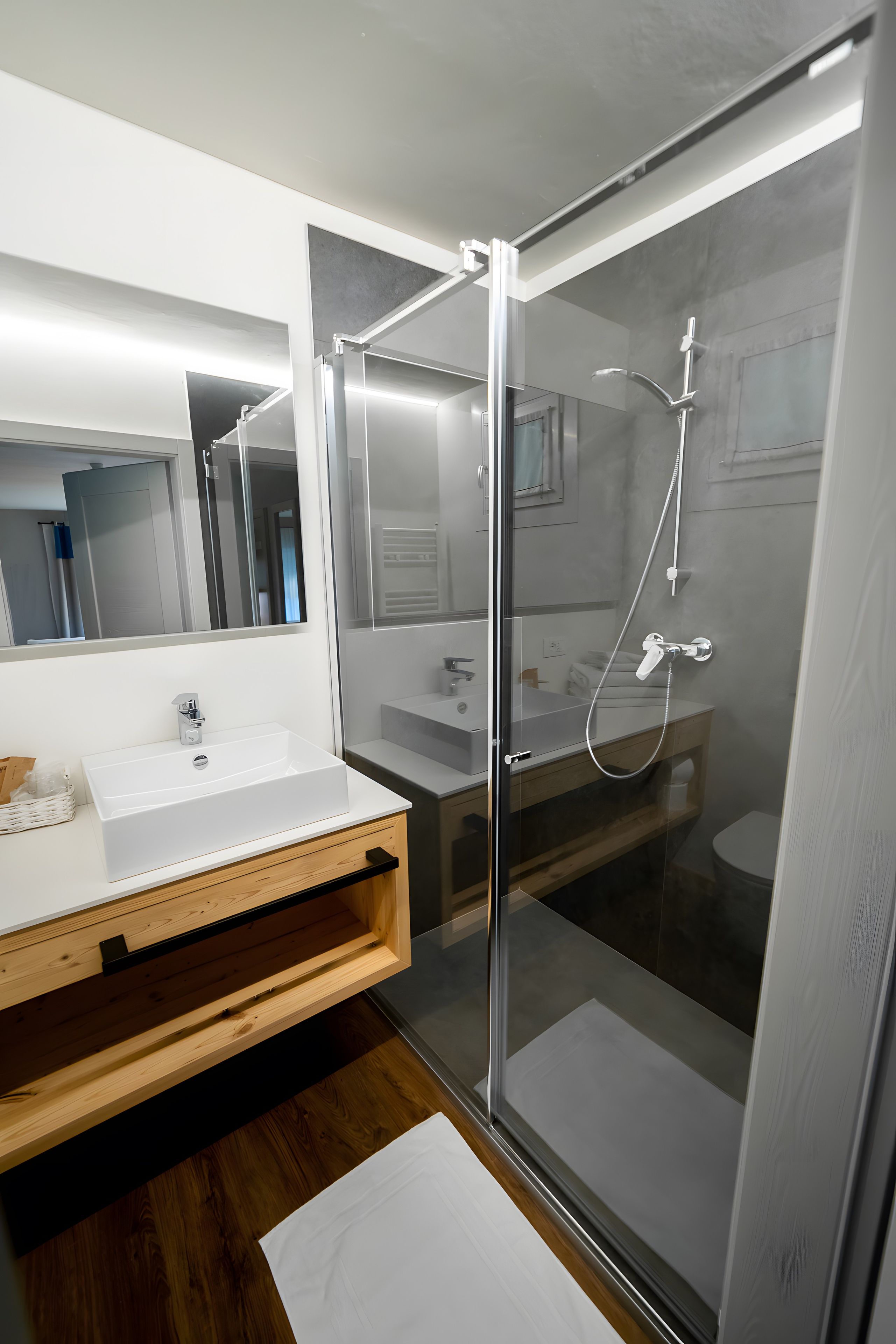 Un baño moderno con ducha de vidrio, tocador de madera y un espejo grande.