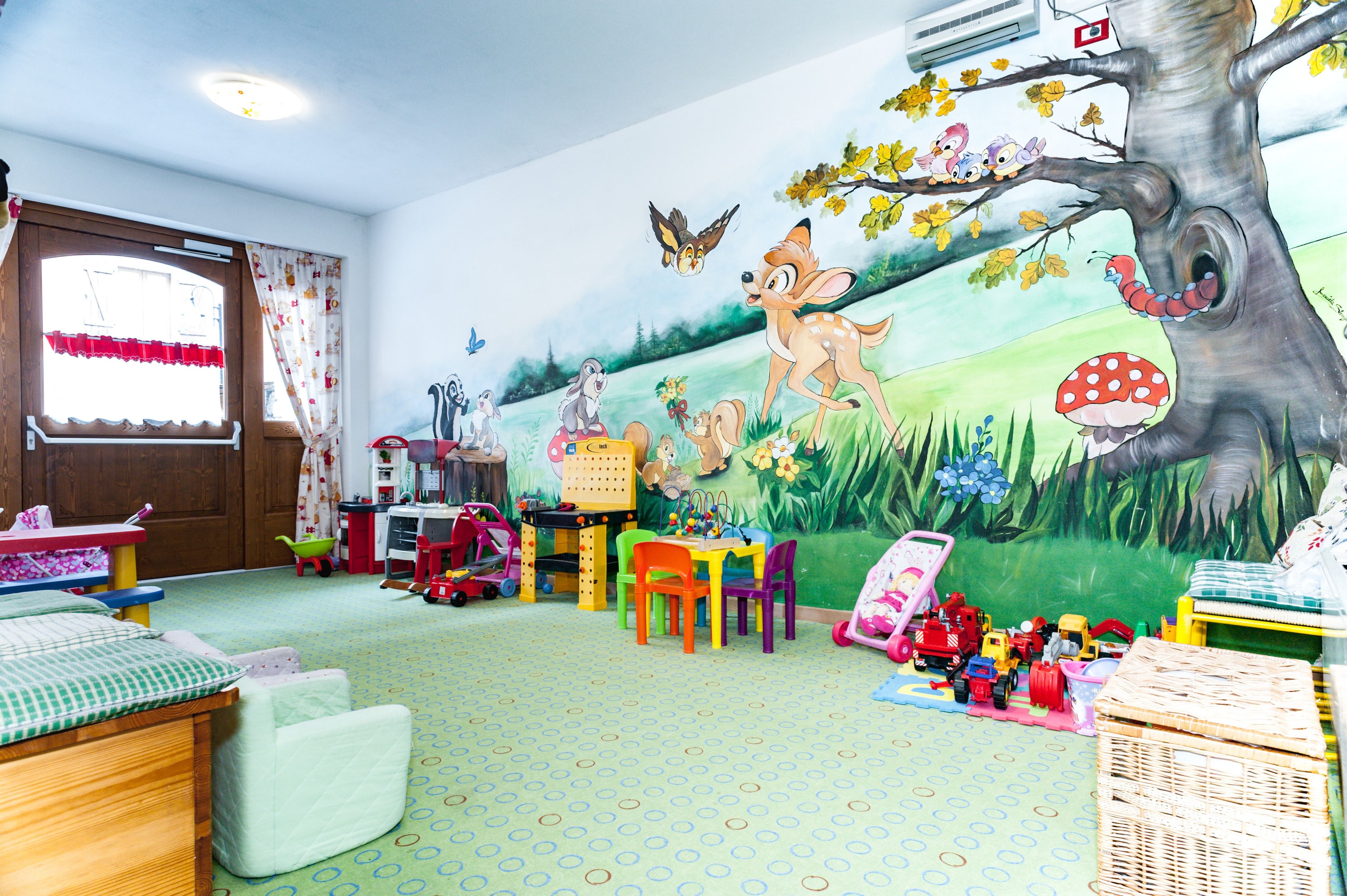 Een kinderspeelkamer met een muurschildering, speelgoed en een groen tapijt.