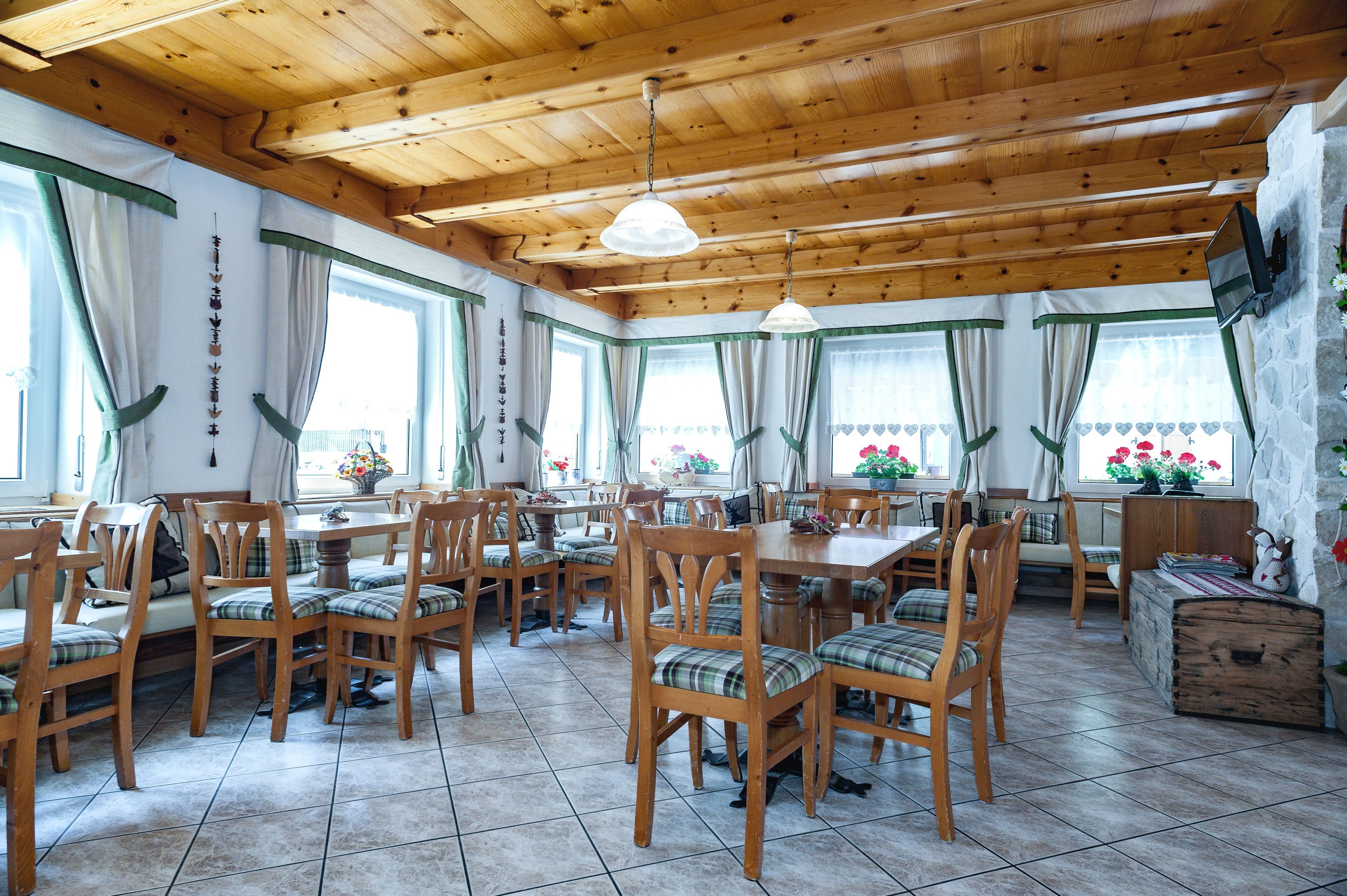 Un comedor con mesas y sillas de madera, ventanas amplias con cortinas y una pared de piedra.