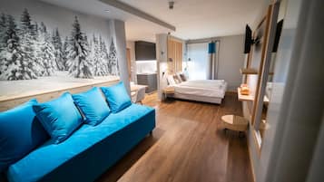 A modern bedroom with a blue sofa, a bed, a desk, and a wall with a forest mural.