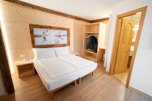 Ein Zimmer mit Holzwänden, einem Bett, einem hölzernen Kopfteil, einem Kleiderständer und einer Tür zu einem anderen Raum.