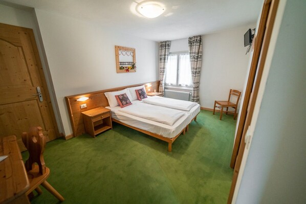 A bedroom with a bed, bedside tables, a chair, a radiator, and a window with curtains. - ‘Sole’ Room with Mountain View, Shared Terrace & Wi-Fi (San Sebastiano)