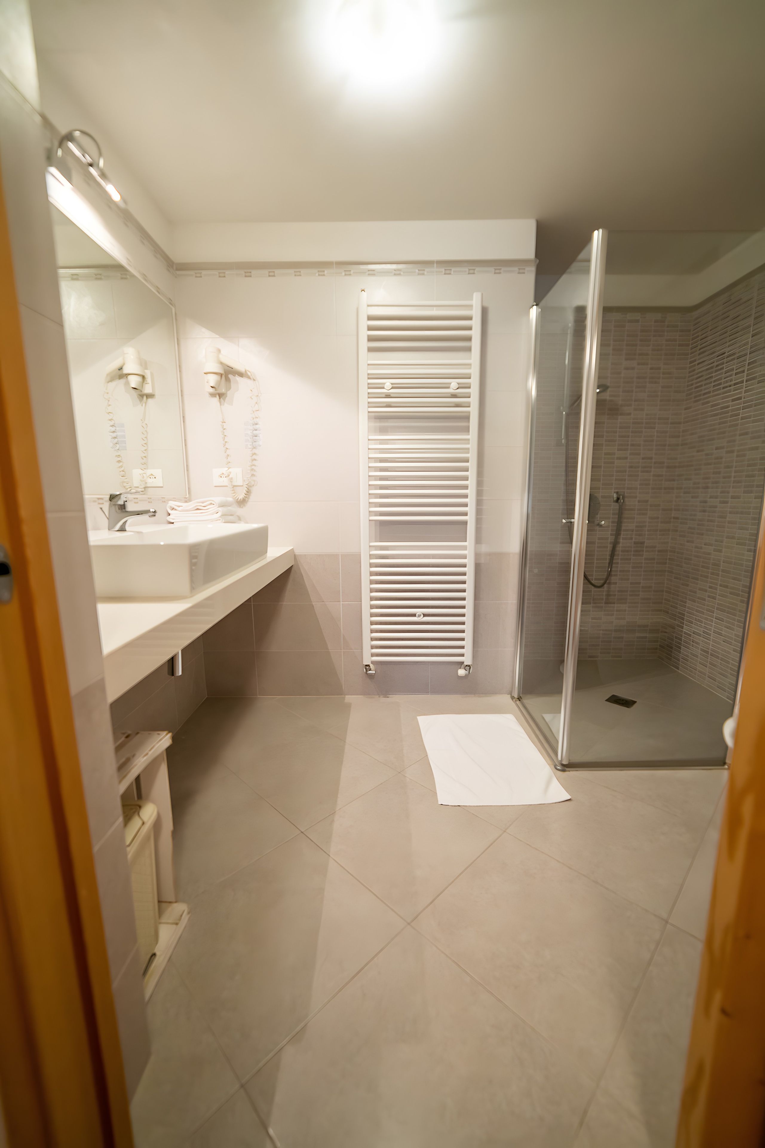 Un bagno moderno con box doccia in vetro, un asciugamano bianco sul pavimento e un portascopevoli.