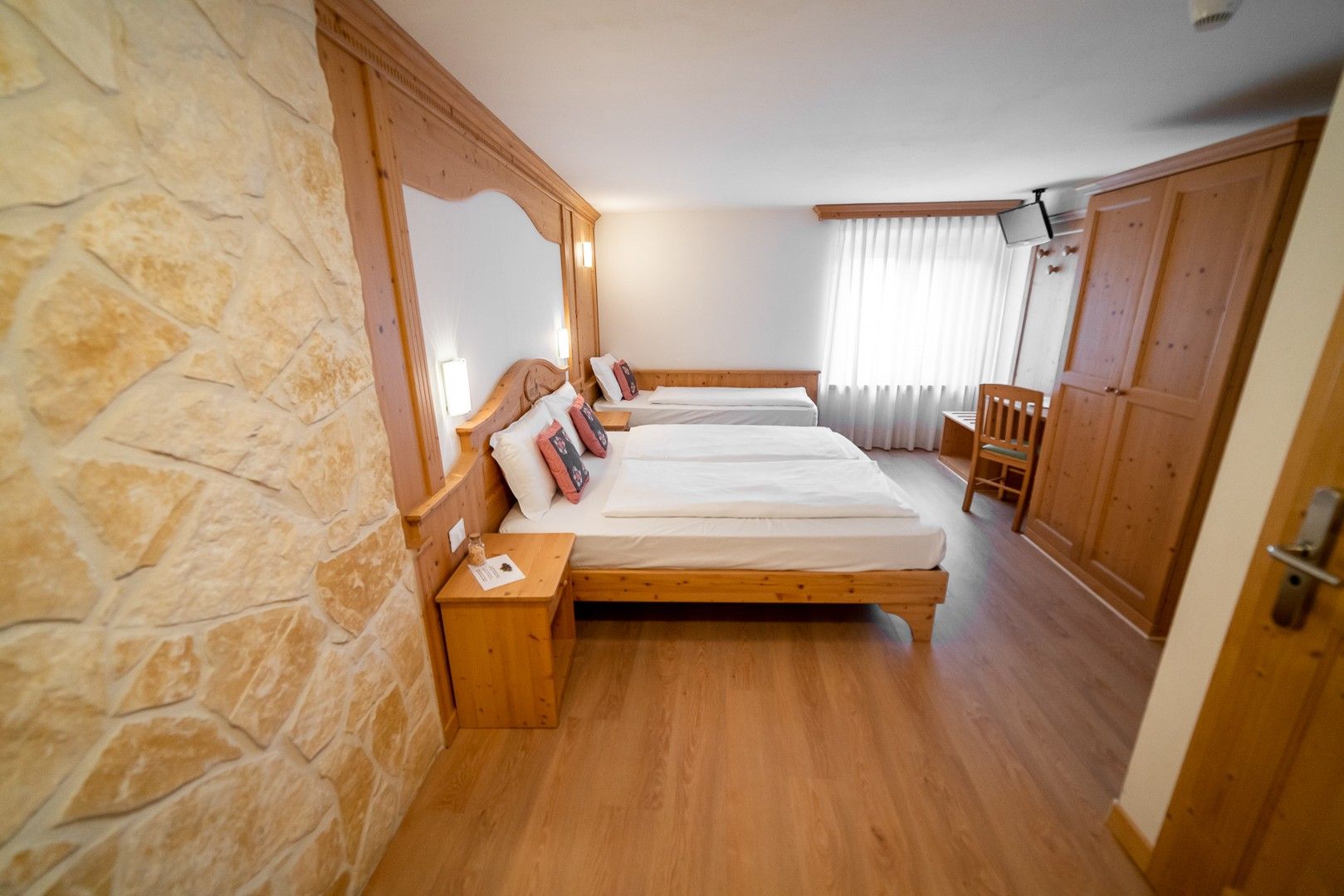 Un dormitorio con dos camas de madera, paredes de piedra, un armario de madera y una silla.