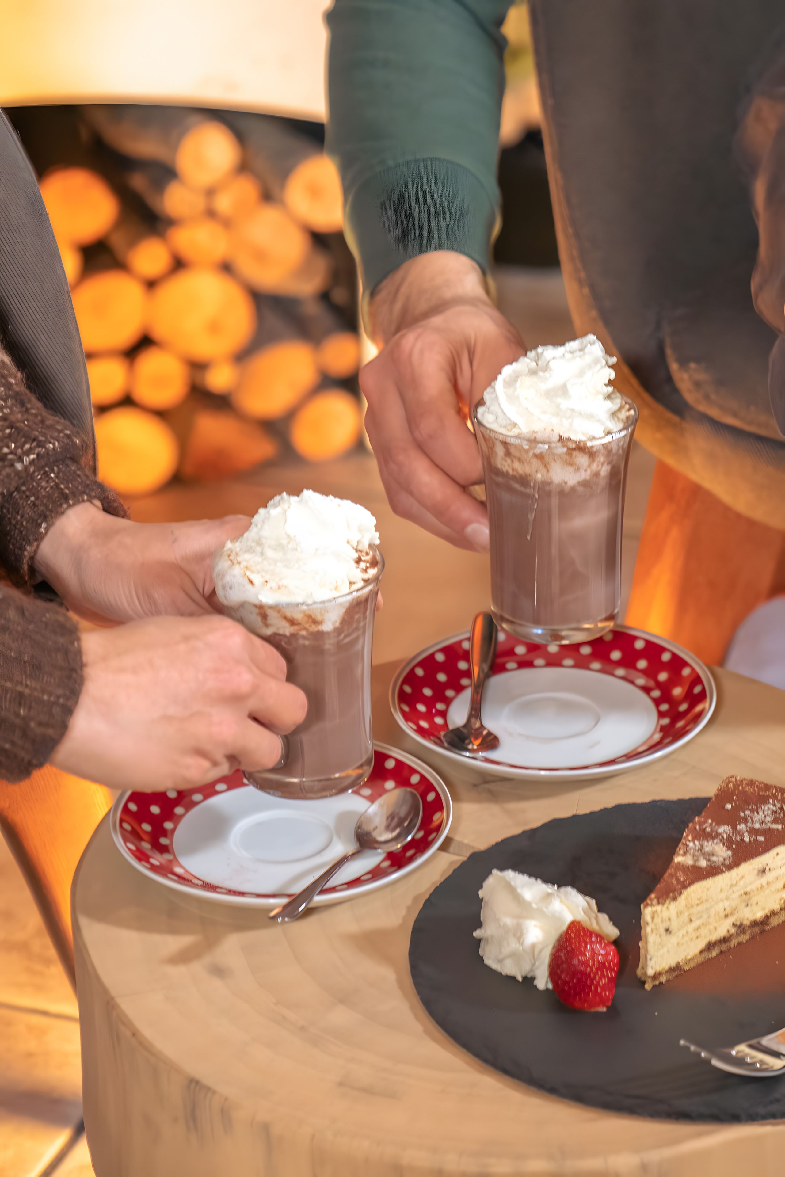 Twee mensen houden glaasjes met een dessert met slagroom vast, met een bord taart en een aardbei op de tafel.