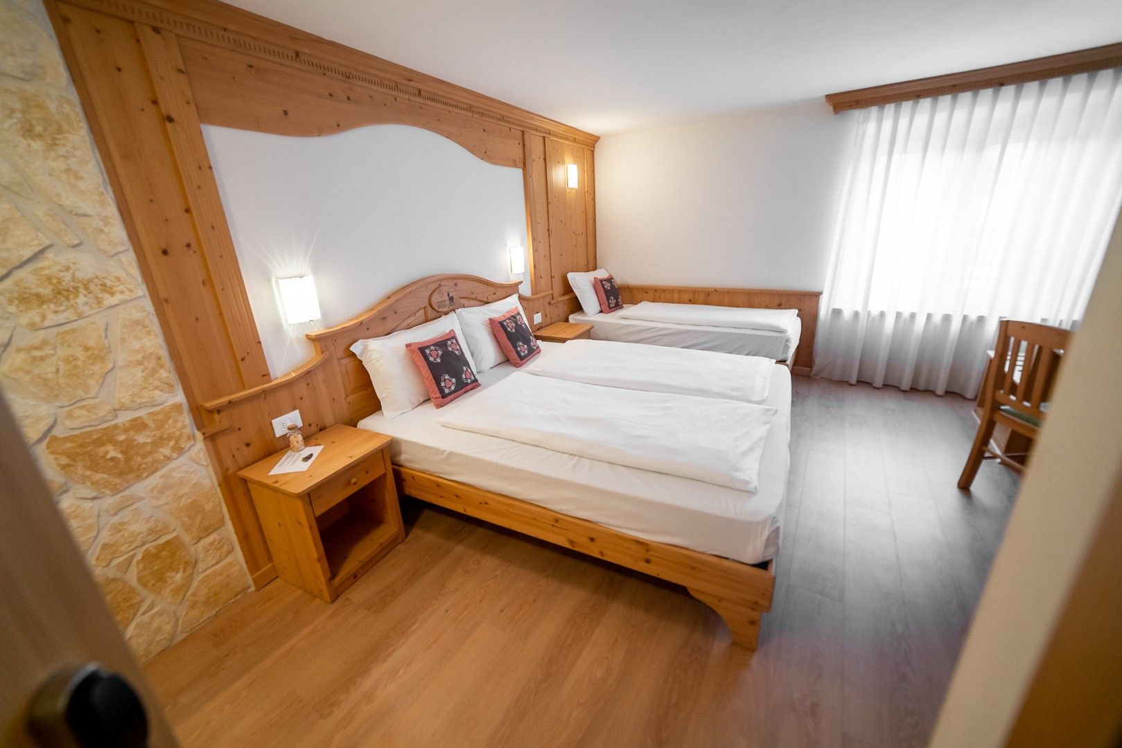 Ein Zimmer mit einem hölzernen Bett, einem Nachttisch, einer Steinsäule und einem Fenster mit Vorhängen.