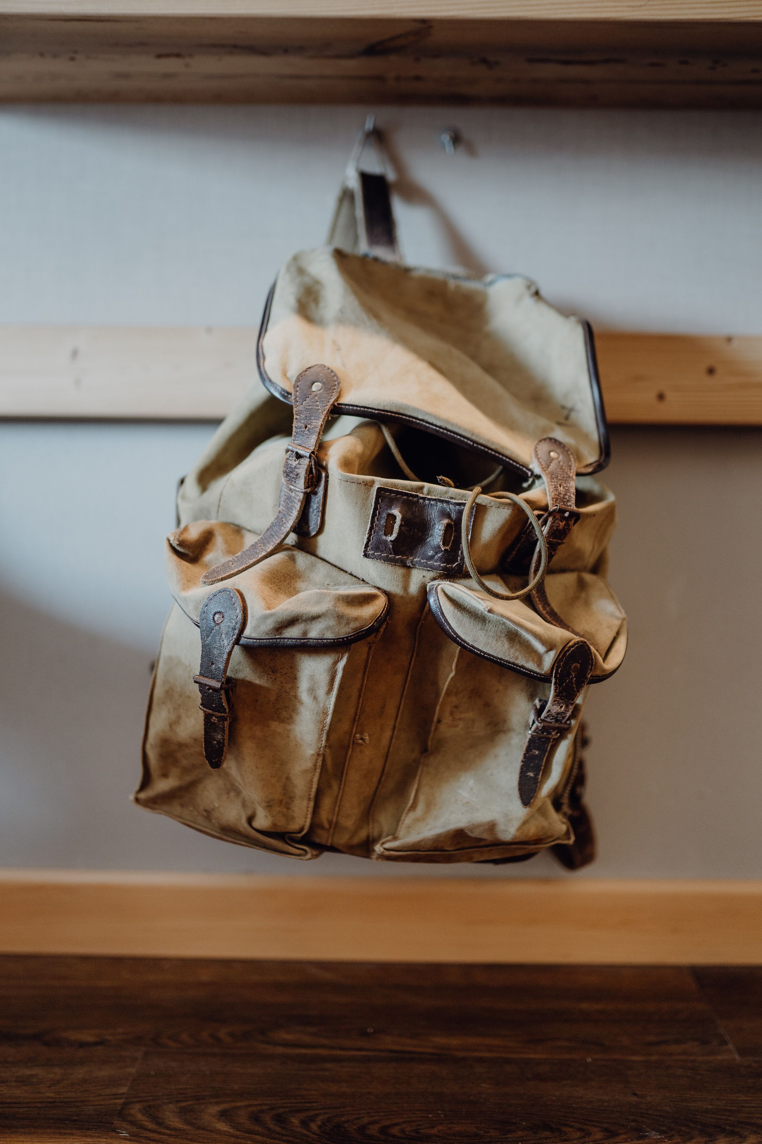 A backpack with multiple compartments and straps, hanging on a wooden shelf.