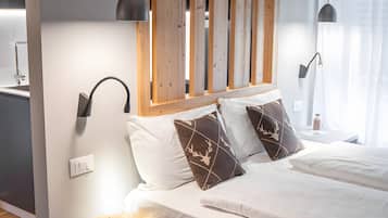 Een moderne slaapkamer met een houten hoofdbord, een rond houten krukje, een bed met wit beddengoed en gestreepte kussens, en twee wandlampen.