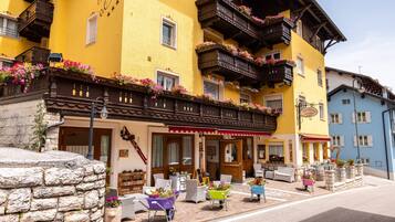 Un hotel con fachada amarilla, balcones de madera con jardineras florales, asientos al aire libre y paredes de piedra.